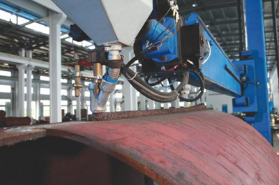 Automatic welding head running a seam on a rolled shell.